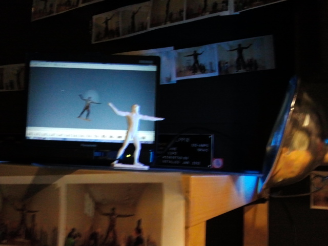 3D Printed "Action Figure" of the Artemision Bronze from the National Archaeology Museum of Athens with the 3D Model running on the screen behind it, and the photography used to print it printed on the walls. 